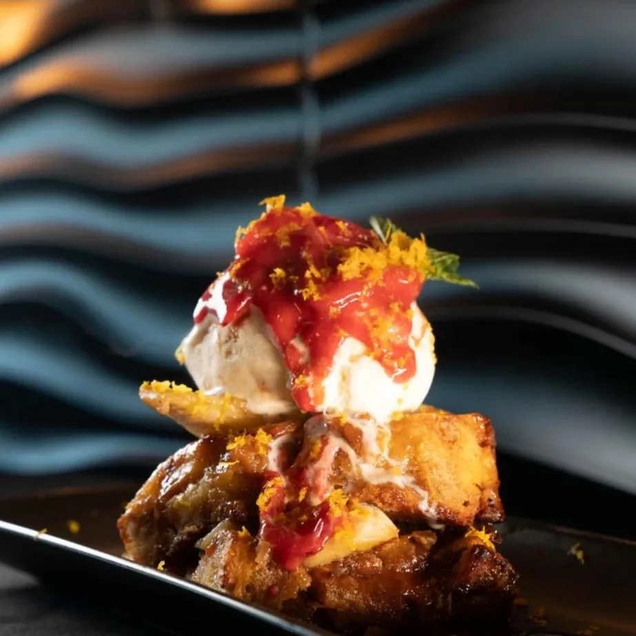 Bread pudding with vanilla ice cream, strawberry sauce and orange zest