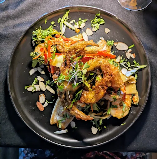 Crispy seafood over noodles with vegetables and sliced almonds