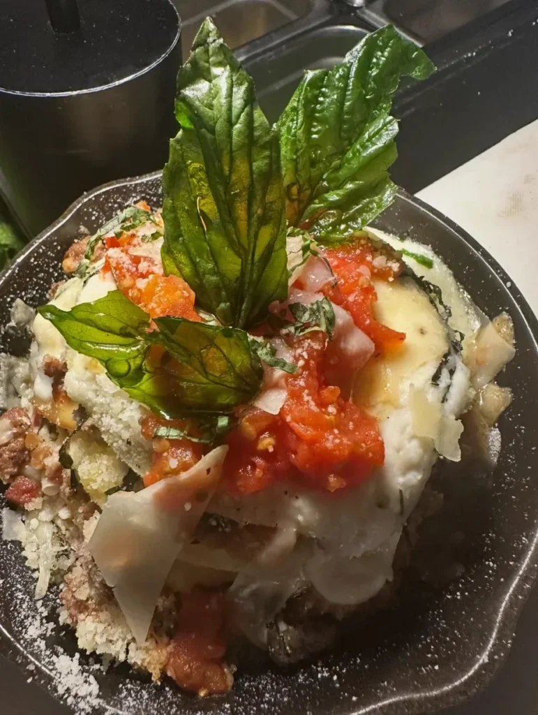 A baked skillet dish with tomato, melted cheese and crispy basil
